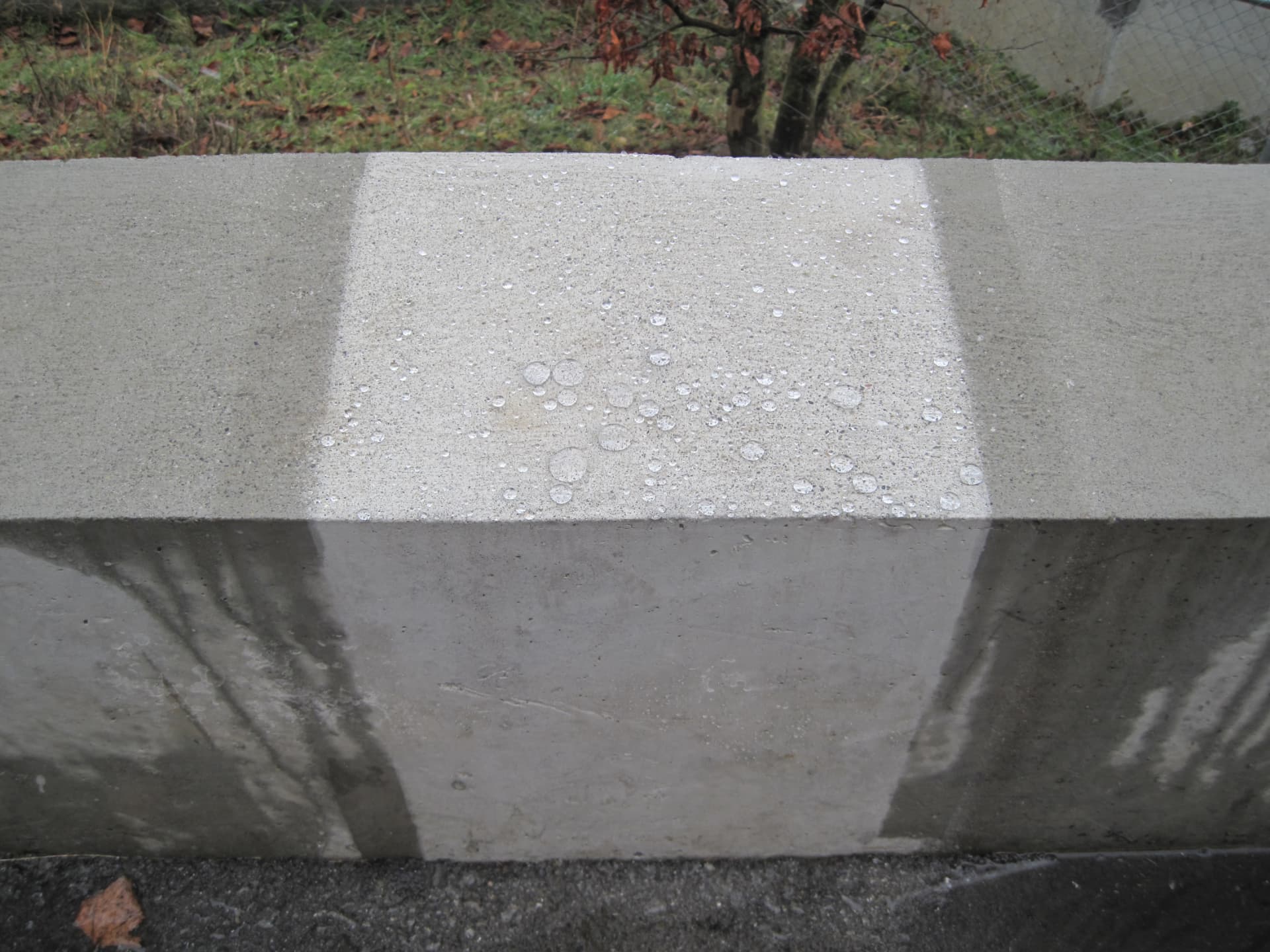Betonmauer, teilweise behandelt: auf der imprägnierten Fläche perlt das Wasser in Tropfen ab, der unbehandelte Bereich saugt es auf und dunkelt nach.